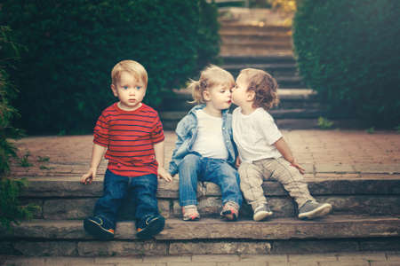 Group of three cute funny adorable white Caucasian children toddlers boys girl sitting together kissing each other. Love jealousy friendship childhood concept. Best friends forever. Toned with retro filters.の写真素材