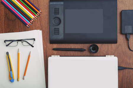 Flat lay of office equipment for working with laptop, graphic tablet, paper, pencils, glasses. Small...
