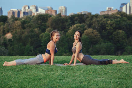 Two young beautiful Caucasian women yogi doing yoga pose. Women doing abs stretching workout in park...
