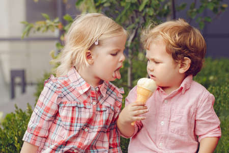 Group portrait of two white Caucasian cute adorable funny children toddlers sitting together sharing ice-cream food. Love friendship concept. Best friends forever.の写真素材