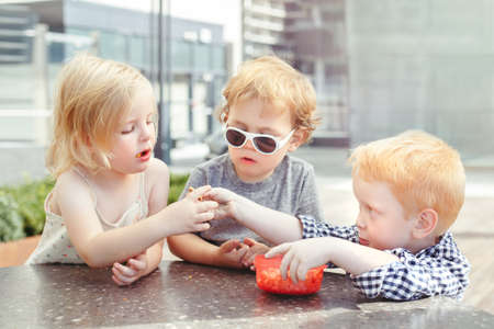Group portrait of three white Caucasian cute adorable funny children toddlers sitting together sharing food. Love friendship childhood concept. Best friends foreverの写真素材