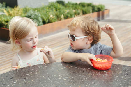 Group portrait of two white Caucasian cute adorable funny children toddlers sitting together sharing eating food. Love friendship childhood concept. Best friends foreverの写真素材