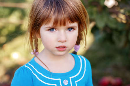 Closeup portrait of cute adorable little red-haired Caucasian girl child with blue eyes looking in...