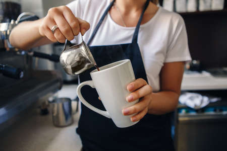 Closeup macro shot of Caucasian woman hands making coffee. Barista pouring hot coffee in white mug cupの写真素材