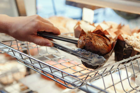 Portrait of  Caucasian waiter barista taking muffin pastry from shop-window. Person at work place, small business conceptの写真素材