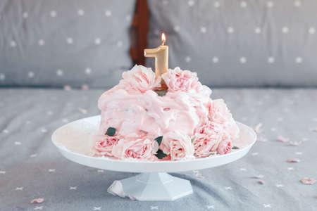 Gourmet pink cake with large natural real rose flowers and candle on stand in bedroom for baby birthday. Home indoors cake-smash first year conceptの写真素材