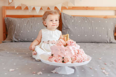Portrait of cute adorable Caucasian blonde baby girl in white dress celebrating her first birthday. Home indoors cake smash first year conceptの写真素材