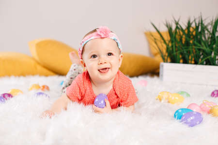 Cute adorable Caucasian baby girl in red t-shirt sitting on white soft fluffy rug carpet in studio....