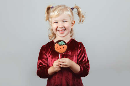 Portrait of adorable funny white blonde Caucasian girl with pigtails dressed for Halloween. Child playing having fun in studio for autumn fall seasonal holiday. Kid eating chocolate lollipopの写真素材