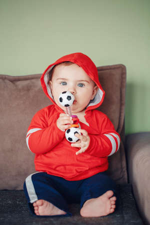 Portrait of cute adorable Caucasian baby boy, wearing red sport hoodie shirt and tracksuit pants....
