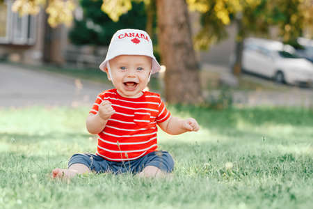 Portrait of little white Caucasian baby boy wearing Canadian hat with maple leaf. Child sitting on...