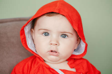 Closeup portrait of cute adorable Caucasian surprised baby boy with blue eyes, wearing red sport...