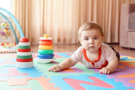 Portrait of cute adorable blond Caucasian smiling child boy with blue eyes lying on floor in kids children room looking in camera. Baby crawling on playmat. Early education developmentの写真素材