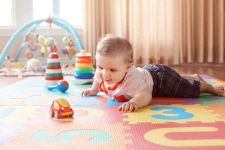 Portrait of cute adorable blond Caucasian smiling child boy with blue eyes crawling on floor in kids...