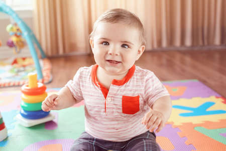 Closeup portrait of cute adorable blond Caucasian smiling child boy with blue eyes sitting on floor...