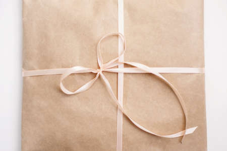 Cardboard carton package wrapped with light brown paper and tied with pink string ribbon in bow....