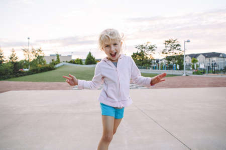 Happy childhood. Portrait of cute adorable little blonde Caucasian girl child making funny silly faces. Kid playing having fun in park outside at sunset. Toned with film filters. の写真素材