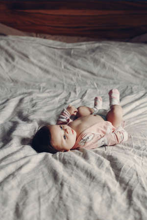 Portrait of cute adorable funny white Caucasian brunette little baby newborn wearing diaper and lying on bed in bedroom. Authentic lifestyle candid real life. Toned with film filters.の写真素材