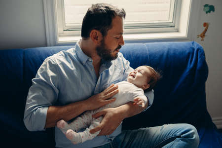 Portrait of middle age Caucasian father trying to calm down newborn baby. Male man parent holding...