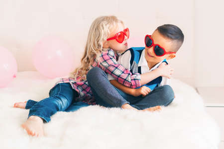 Portrait of two happy white Caucasian cute adorable funny children wearing heart shape glasses. Girl trying to kiss a boy. Love, friendship and fun. Valentine day holiday celebration.の写真素材