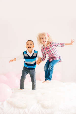 Group portrait of two happy white Caucasian cute adorable funny children jumping on bed in bedroom. Boy and girl having fun together. Best friends forever.の写真素材