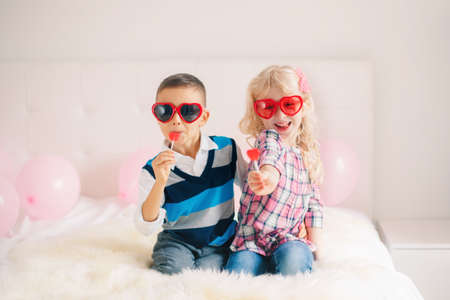 Group portrait of two happy white Caucasian cute adorable funny children eating heart shaped lollipops. Boy and girl celebrating Valentine Day. Love, friendship and fun. Best friends forever.の写真素材