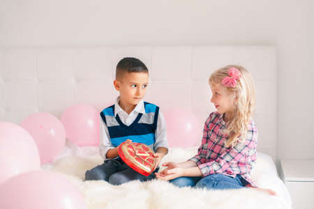 Group portrait of two Caucasian cute adorable children eating heart shaped candies. Boy giving girl chocolate gift present to celebrate Valentine Day. Love and friendship concept. Best friends foreverの写真素材