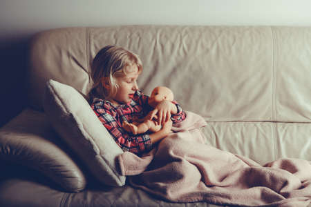 Child playing with toy. Cute Caucasian girl holding cuddling with baby doll. Kid lying in bed at...
