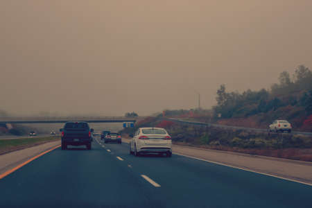 Traffic on highway in fog mist. Cars on freeway road at evening in american city country. Poor...