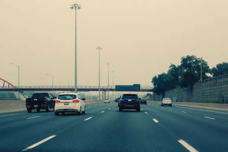 Traffic on highway in fog mist. Cars on freeway road at evening in american city country. Poor visibility in bad weather conditions. Toned wit vintage film hipster filters.の写真素材