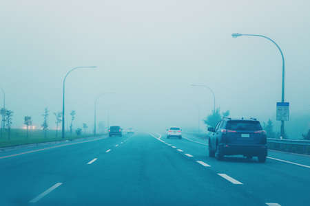 Highway in mystic fog mist smog. Cars on freeway road at evening in american city country. Poor...
