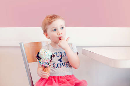 Cute adorable funny Caucasian blonde babyl girl child with blue eyes eating ice cream in large...