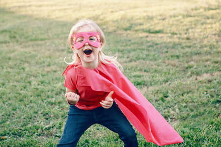 Smiling laughing preschool Caucasian child playing superhero in costume. Girl kid wearing pink mask...