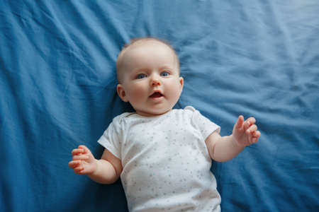 Portrait of cute adorable smiling white Caucasian baby girl boy with blue eyes four months old lying on bed in bedroom looking at camera. View from top above. Happy childhood lifestyle.の写真素材