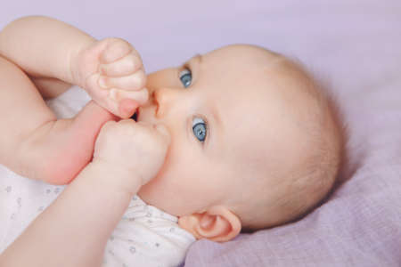 Closeup portrait of cute adorable white Caucasian infant child girl boy with blue eyes lying on bed...