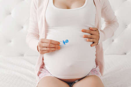Closeup shot of white Caucasian pregnant woman belly with cute tiny newborn pacifier. Expecting...