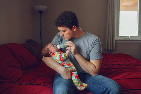 Young Caucasian father feeding newborn baby son daughter with milk. Male man parent holding child on...