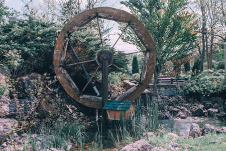 Water wooden old wheel mill in country village near pond stream. Retro vintage machinery in idyllic...