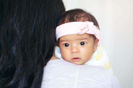Closeup portrait of cute adorable awake Asian Chinese mixed race newborn baby girl with open eyes lying on parent shoulder. Healthy happy childhood ethnic diversity lifestyle. Mothers day.の写真素材