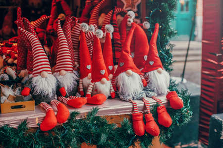 Colorful red toys dwarfs gnomes in red caps hats sitting on counter at traditional holiday Christmas market outdoors. Popular attraction for winter celebration activities. の写真素材