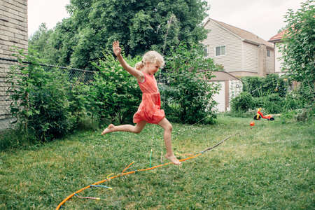 Preschool kids girl splashing with gardening hose sprinkler on backyard during summer day. Child...