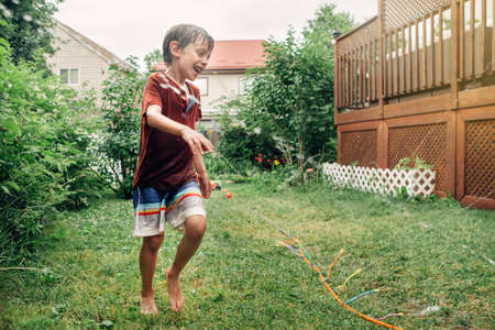 Preschool kid boy splashing with gardening hose sprinkler on backyard during summer day. Child...