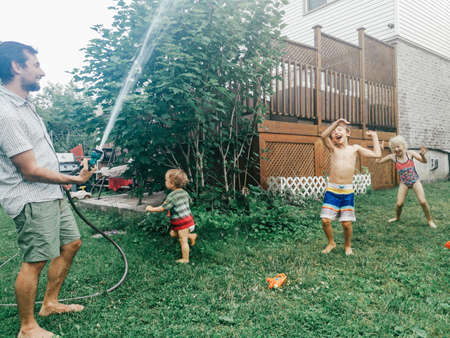 Father man spray shower from hose on kids. Boy girl friends siblings splashing playing under water...