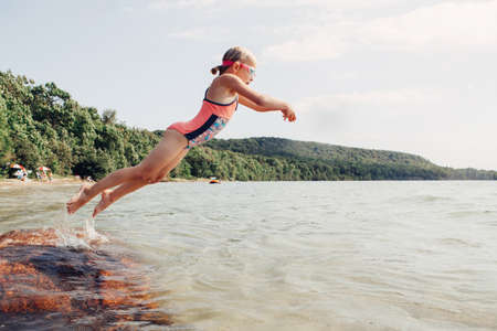Cute funny Caucasian girl swimming in lake river with underwater goggles. Child diving in water on beach. Authentic real lifestyle happy childhood. Summer fun outdoor aquatic activity.の写真素材