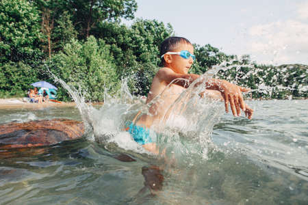 Funny Caucasian boy swimming in lake river with underwater goggles. Child diving in water with splash on beach. Authentic real lifestyle happy childhood. Summer fun outdoor aquatic activity.の写真素材