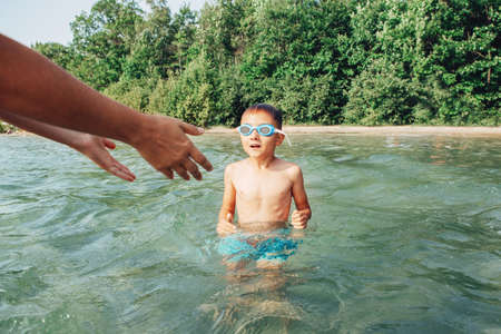 Parent teaching training helping son learn to swim. Child in swimming goggles diving in water on...