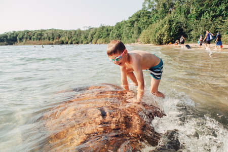 Cute funny Caucasian boy swimming in lake river with underwater goggles. Child diving in water on beach. Authentic real lifestyle happy childhood. Summer fun outdoor aquatic activity.の写真素材
