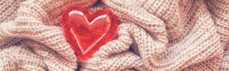 Closeup macro of knitted wool fabric material with red shiny smooth heart. Clothing texture background with wrinkles and folds. Valentine holiday love card. Web banner for website header.の写真素材
