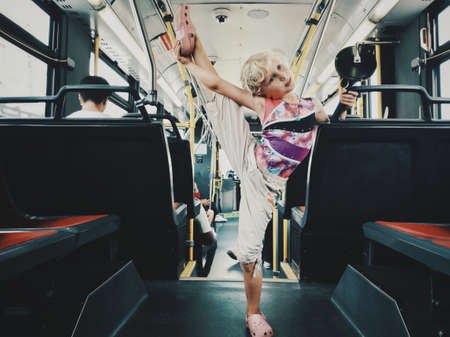 Toronto, Ontario, Canada - September 11, 2019: Funny blonde Caucasian girl riding on a bus and stretching before gymnastics class. Recreational sport for kids. Happy childhood lifestyle.の写真素材