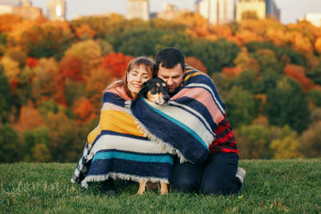 Beautiful young couple with dog in park. Man and woman hugging playing with their domestic animal...